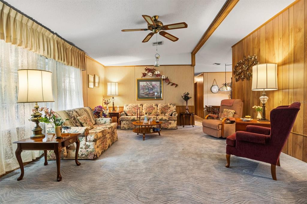 A living room features wood-paneled walls, floral sofas, a burgundy armchair, and patterned gray carpet — 6775 BRENTWOOD DRIVE NE, WINTER HAVEN, FL