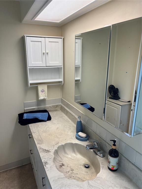 A bathroom features a shell-shaped sink, marble-look countertop, white cabinetry, and a large wall mirror — 3417 N CITRUS CIRCLE UNIT 1633, ZELLWOOD, FL
