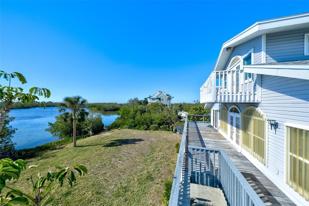 An elevated wooden deck overlooks a grassy yard, palm tree, and a body of water — 145 BURNS ROAD, TERRA CEIA, FL