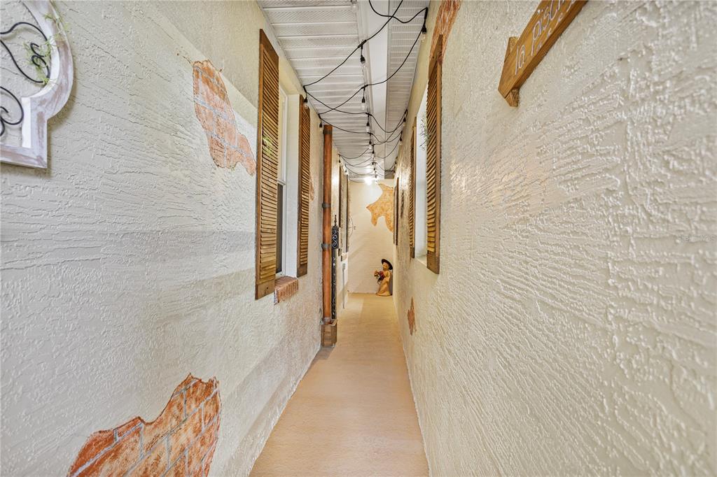 A narrow outdoor walkway features textured walls with faux brick accents and string lights overhead — 14612 BRAY ROAD, ORLANDO, FL