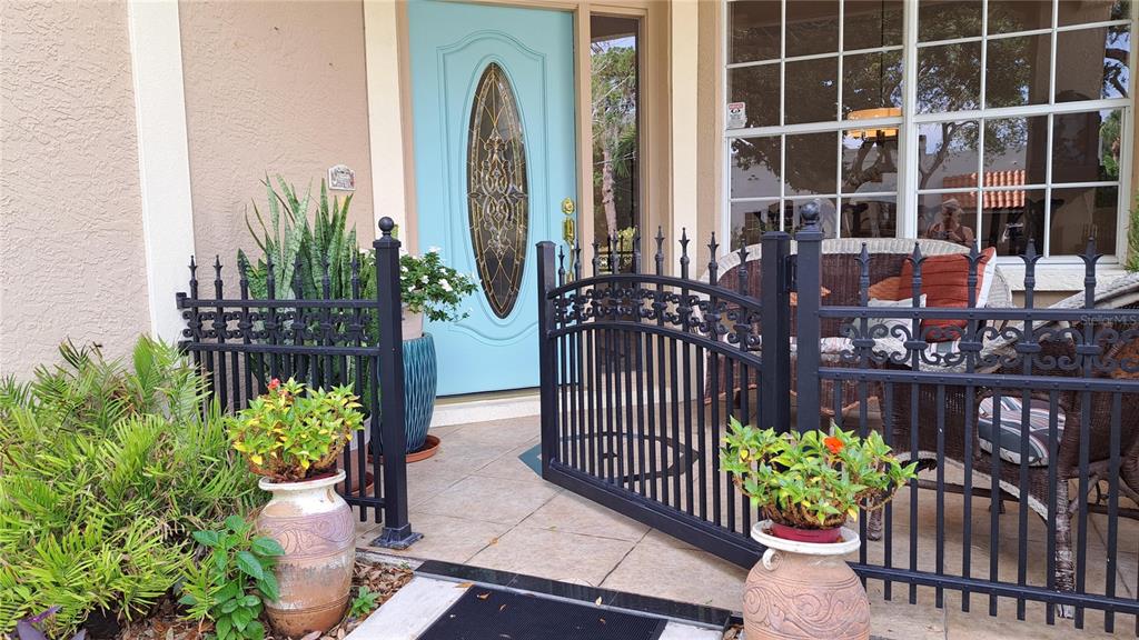 A light blue front door is framed by a black metal fence and potted plants — 2377 BURTON LANE, SARASOTA, FL