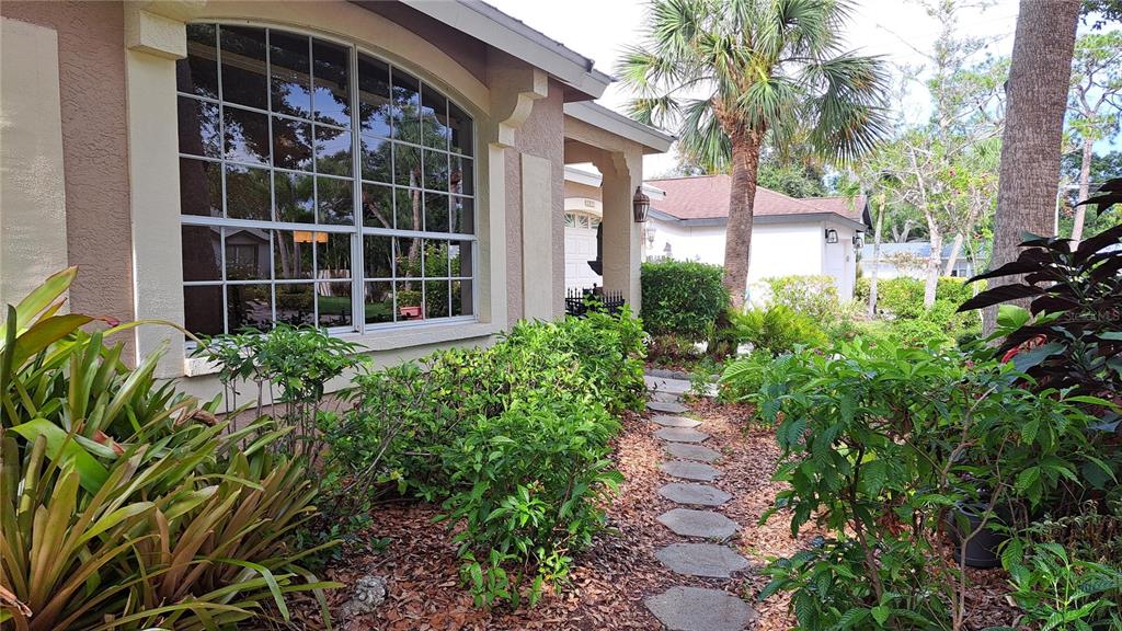 A stone path leads past a large arched window and landscaping toward a house entrance — 2377 BURTON LANE, SARASOTA, FL