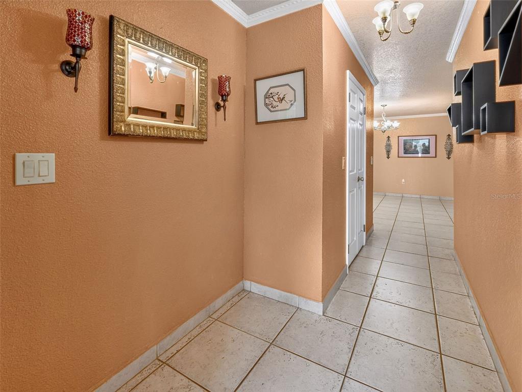 A tiled hallway features peach-colored walls, a gold-framed mirror, wall sconces, and black shelving — 8516 TWIN LAKE BLVD, TAMPA, FL