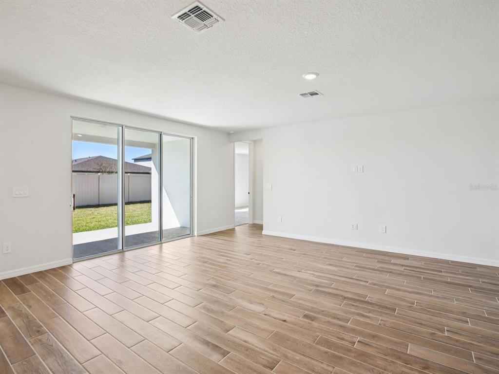 A bright living room features wood-look tile flooring, white walls, and sliding glass patio doors — 97 TEQUESTA COURT, PALM COAST, FL