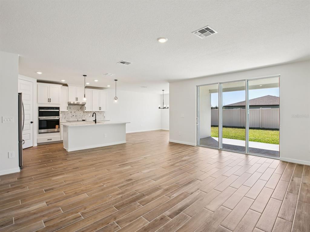 A bright open-concept kitchen and living area with wood-look tile flooring and sliding glass doors — 97 TEQUESTA COURT, PALM COAST, FL