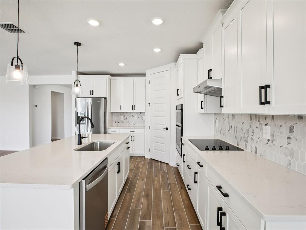 A modern kitchen features white cabinetry, quartz countertops, a large island, and wood-look tile flooring — 97 TEQUESTA COURT, PALM COAST, FL
