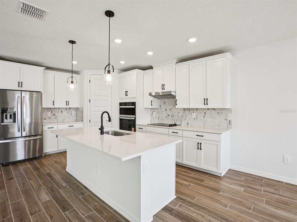 A modern kitchen features white cabinetry, a central island with a sink, and wood-look flooring — 97 TEQUESTA COURT, PALM COAST, FL