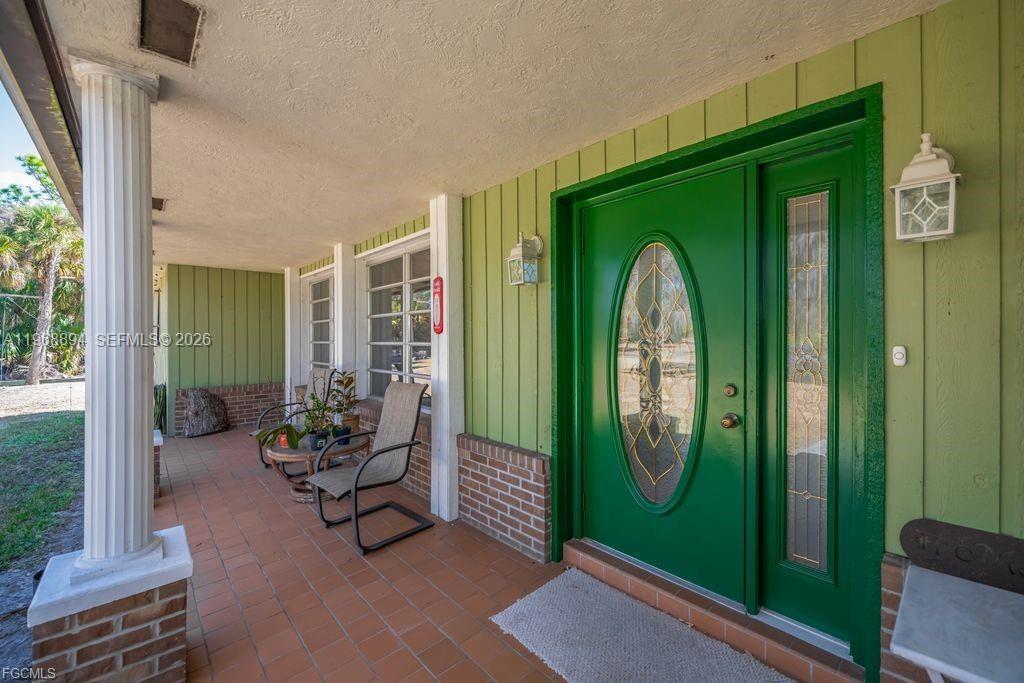 A covered porch features green vertical siding, a bright green front door, and tiled flooring — 1209 County Rd 78, La Belle FL 33935, LA BELLE, FL