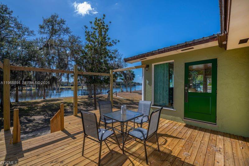 A wooden deck features a small dining set overlooking a lake and trees — 1209 County Rd 78, La Belle FL 33935, LA BELLE, FL