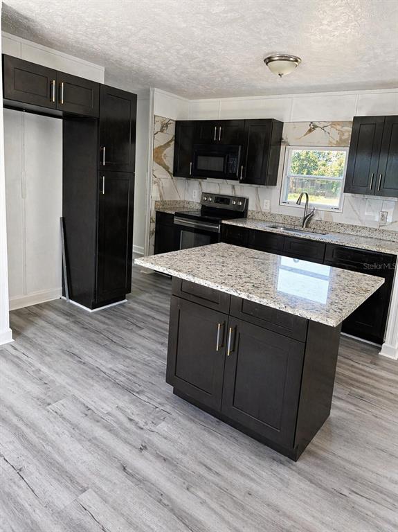 A kitchen features dark cabinets, granite countertops, a center island, and light wood-look flooring — 4521 DUNKELD AVENUE, ORLANDO, FL