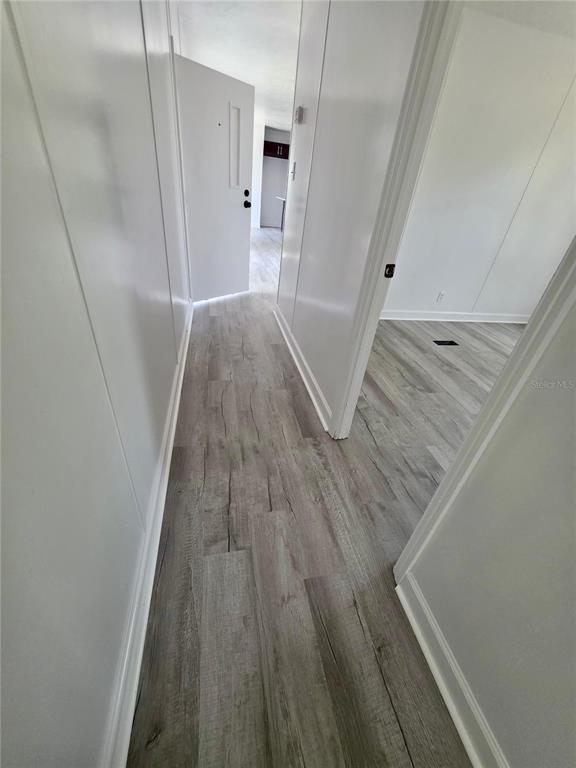 A hallway with light-colored wood-look flooring leads toward an open doorway and a white door — 4521 DUNKELD AVENUE, ORLANDO, FL