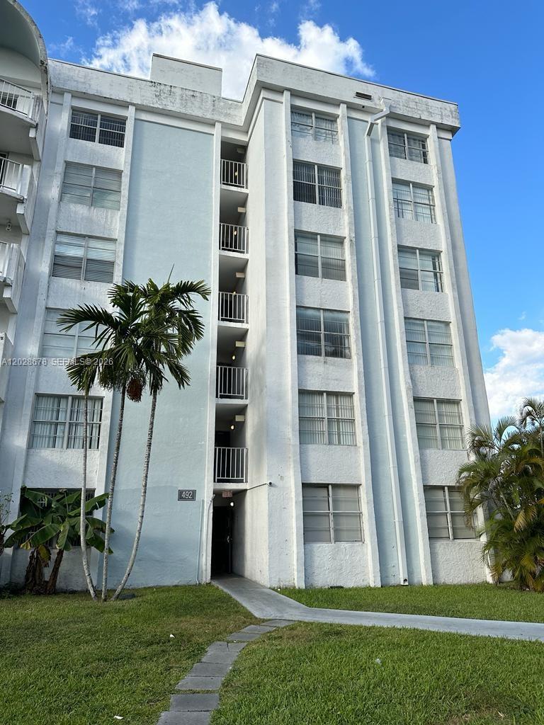 A multi-story white apartment building features a central stairwell with balconies and palm trees — 492 NW 165th St Rd # 211, Miami FL 33169, MIAMI, FL