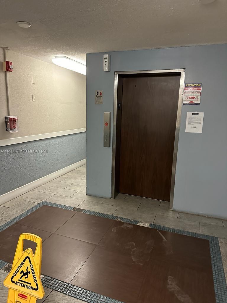 An elevator with a wood-look door is located in a hallway with tiled floors — 492 NW 165th St Rd # 211, Miami FL 33169, MIAMI, FL