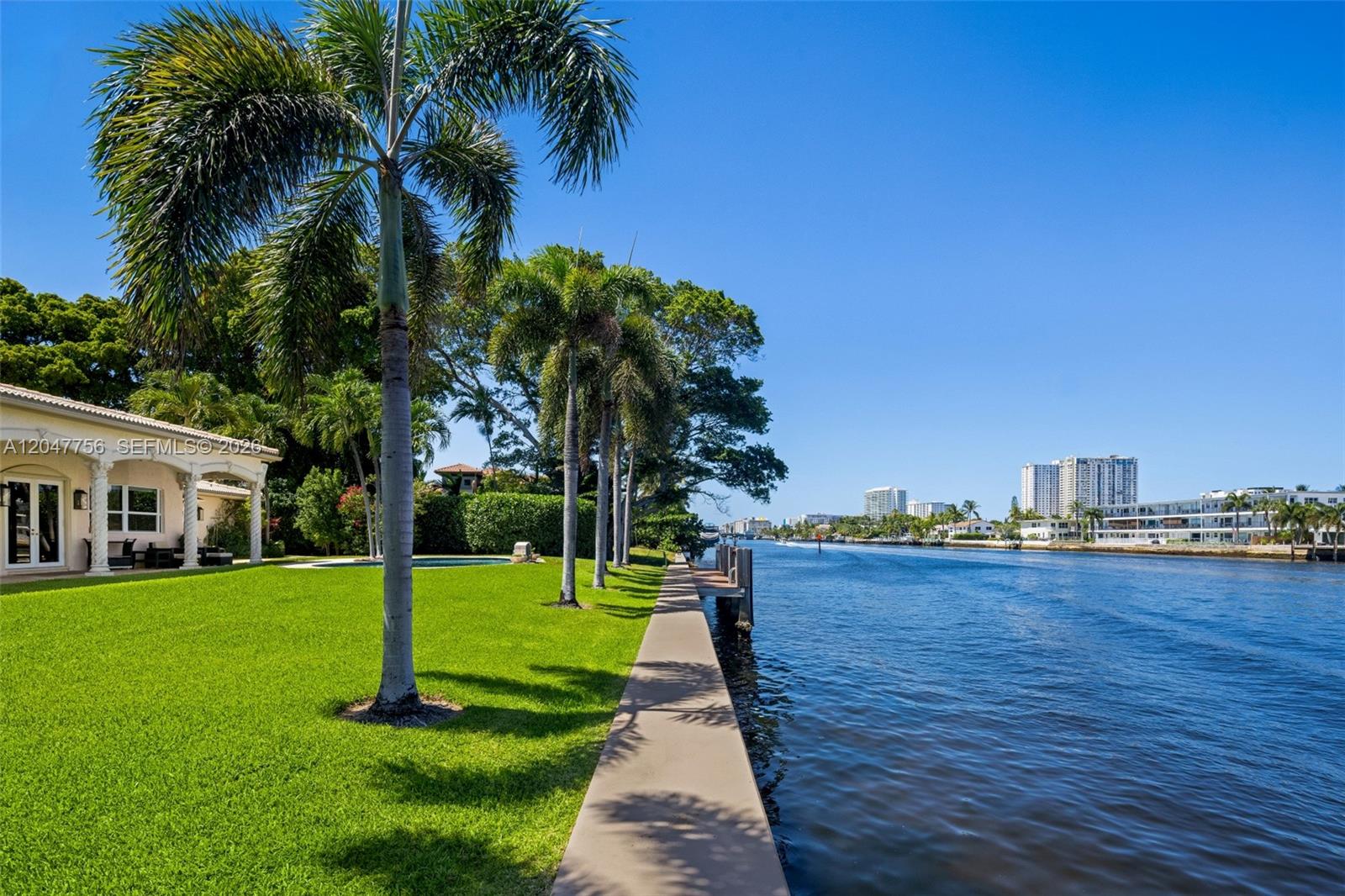 A waterfront backyard features a manicured lawn, palm trees, a concrete walkway, and a dock — 600 SE 28th Ave, Pompano Beach FL 33062, POMPANO BEACH, FL