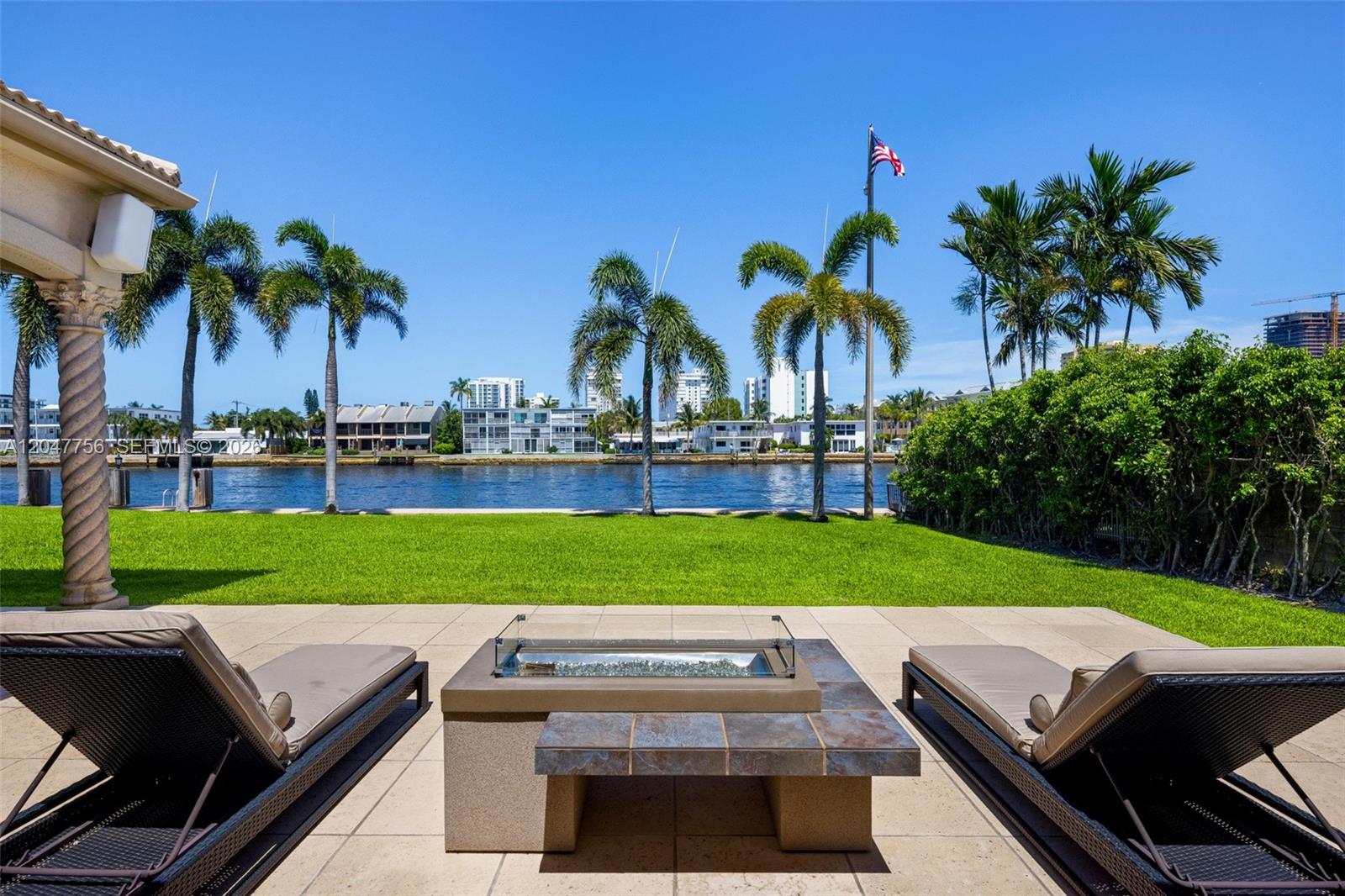 A patio with two lounge chairs and a fire pit overlooks a lawn and waterway — 600 SE 28th Ave, Pompano Beach FL 33062, POMPANO BEACH, FL