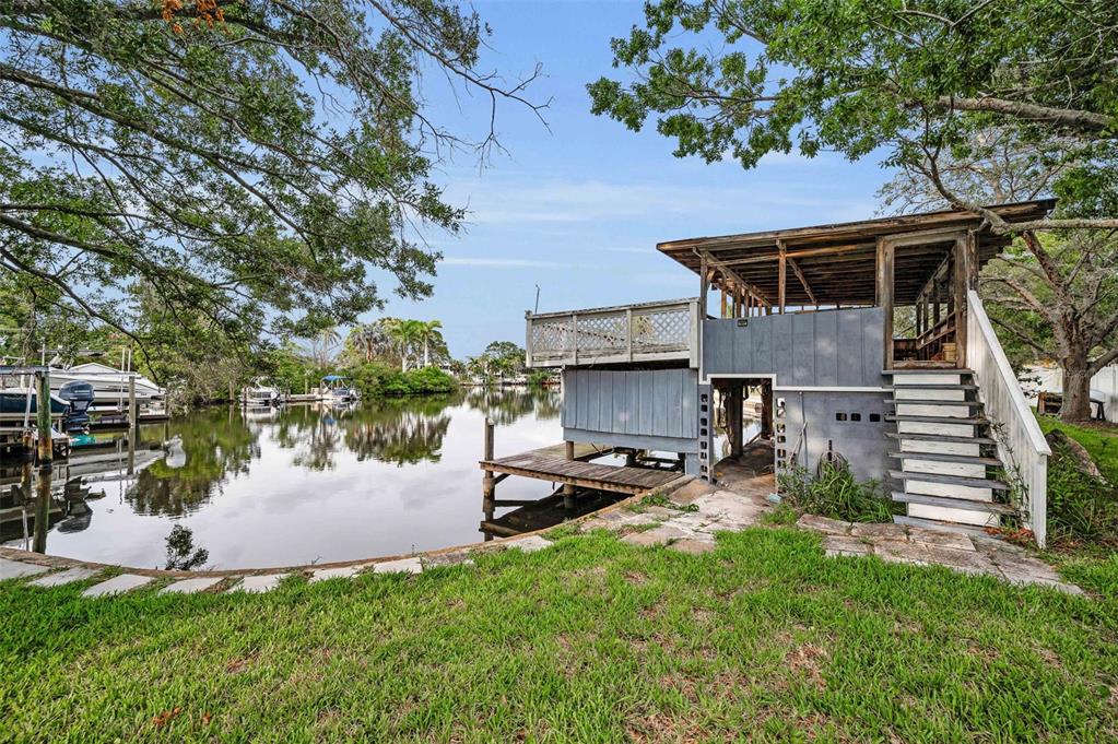 A two-story waterfront structure with a wooden deck and stairs sits beside a canal — 394 GEORGIA AVENUE, CRYSTAL BEACH, FL