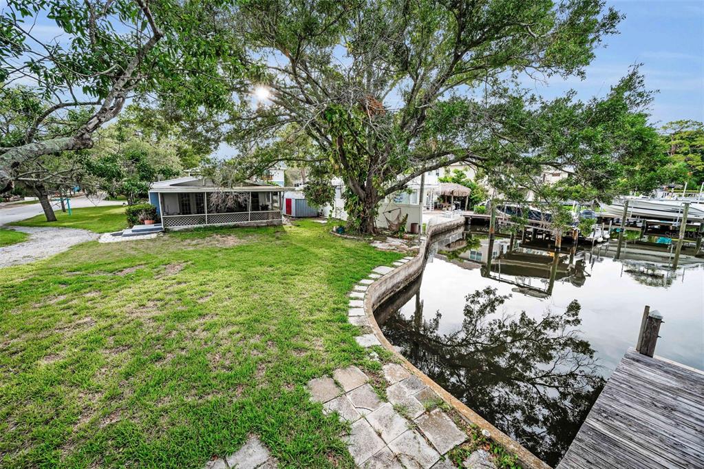 A grassy backyard features a small house, a large tree, and a canal with docks — 394 GEORGIA AVENUE, CRYSTAL BEACH, FL