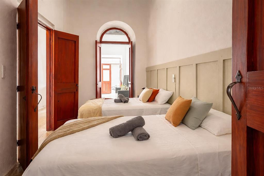 A bedroom with two beds, white walls, and an arched doorway leading to a courtyard — 54 CALLE CRUZ UNIT 54, SAN JUAN, PR