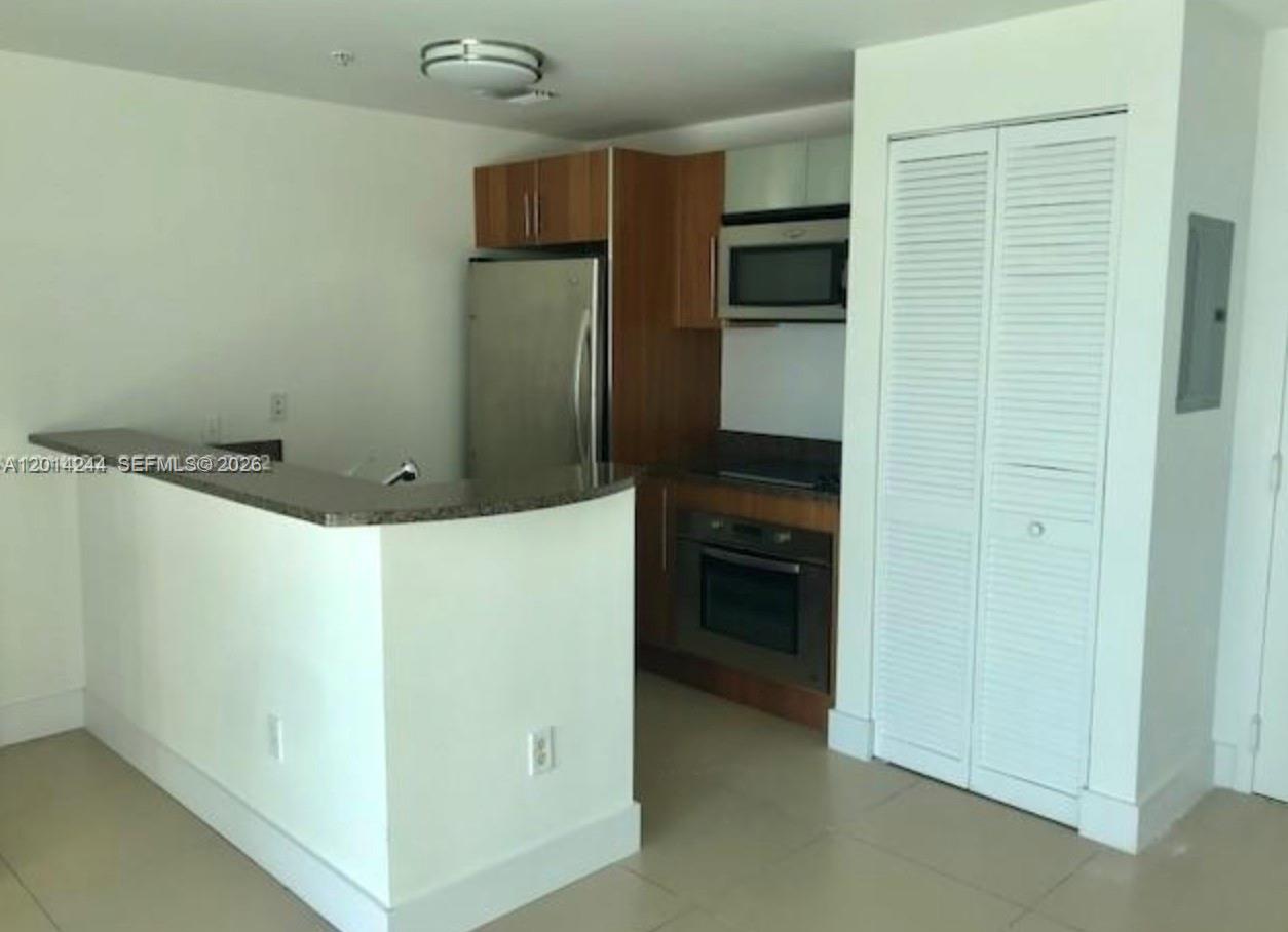 A kitchen features wood cabinets, stainless steel appliances, and a curved granite breakfast bar — 300 S Biscayne Blvd # L32, Miami FL 33131, MIAMI, FL