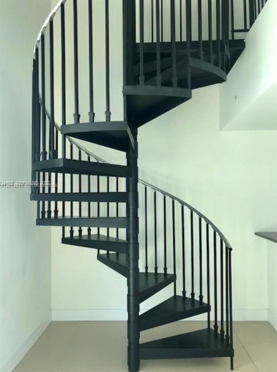 A black metal spiral staircase stands against a plain white wall in a room — 300 S Biscayne Blvd # L32, Miami FL 33131, MIAMI, FL