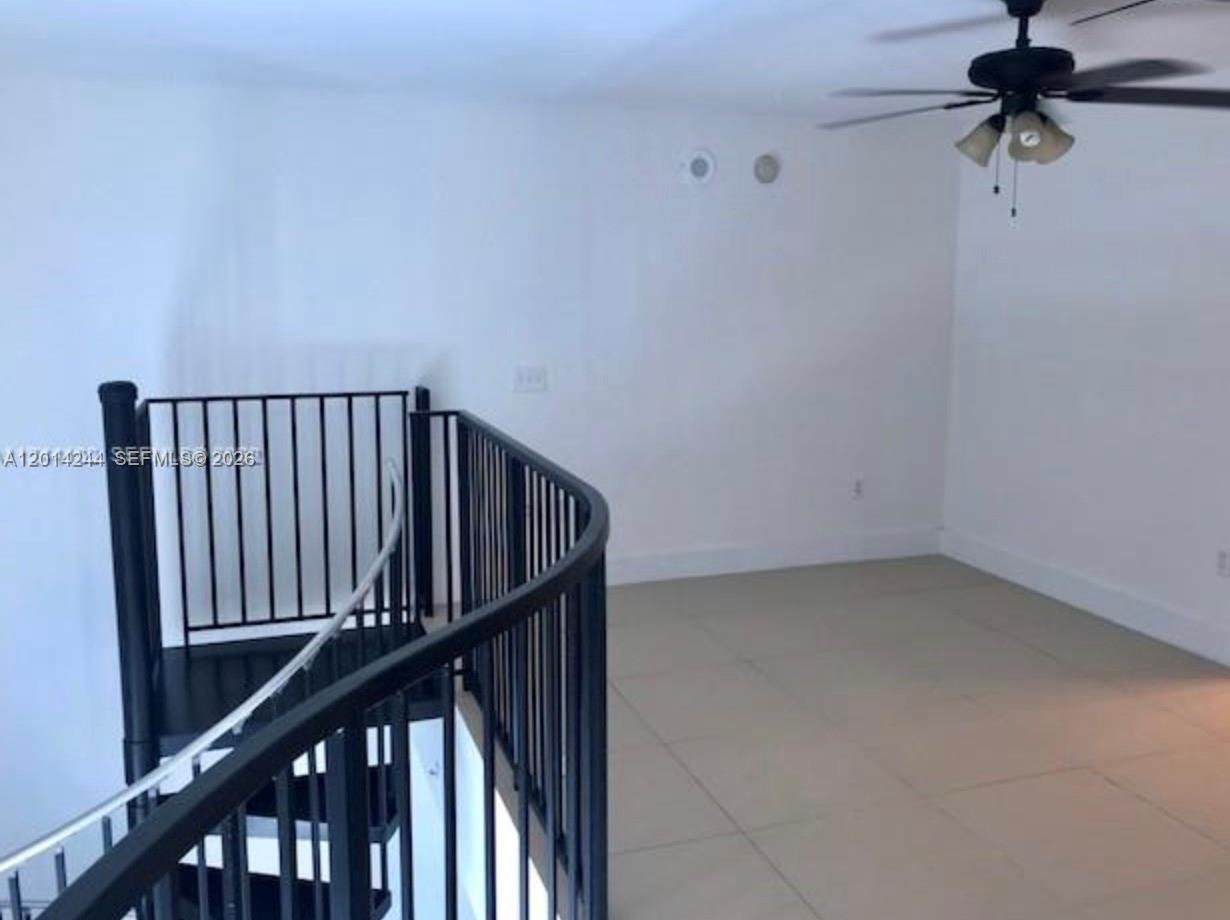 An interior view shows a tiled loft area with a black spiral staircase and railing — 300 S Biscayne Blvd # L32, Miami FL 33131, MIAMI, FL