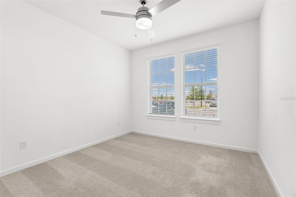 An empty bedroom features white walls, beige carpet, a ceiling fan, and two windows — 1700 RANCH ROAD UNIT A3-2117, NOKOMIS, FL