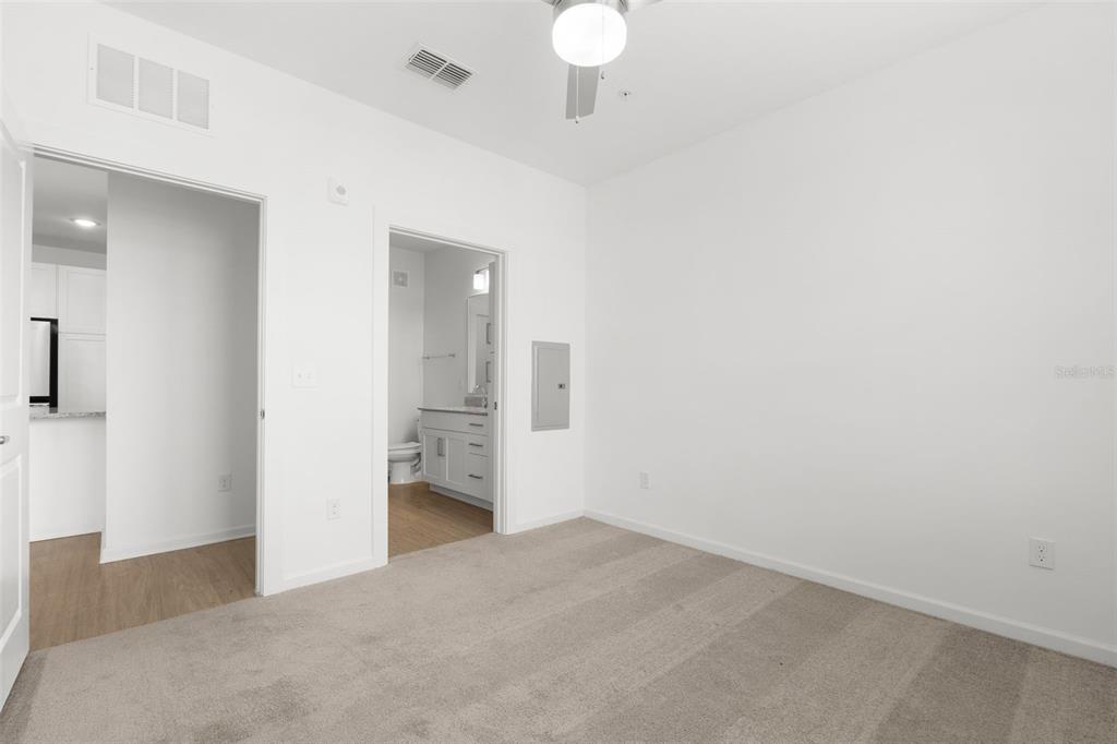 A carpeted bedroom features a ceiling fan, a doorway to a bathroom, and a kitchen view — 1700 RANCH ROAD UNIT A3-2117, NOKOMIS, FL