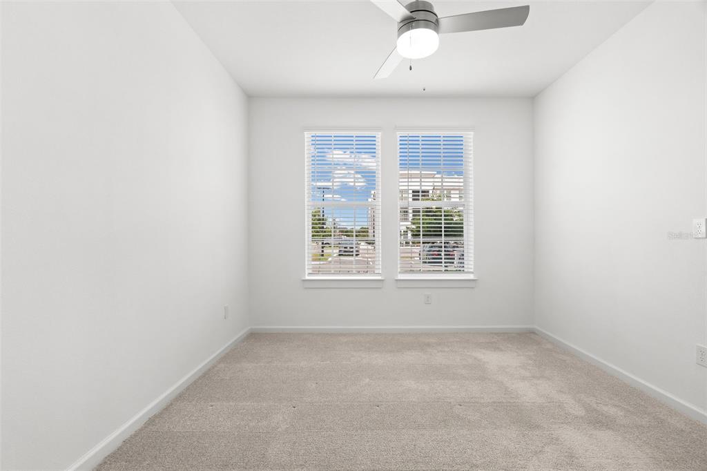A bright, empty bedroom features white walls, beige carpeting, a ceiling fan, and two windows — 1700 RANCH ROAD UNIT A3-2117, NOKOMIS, FL
