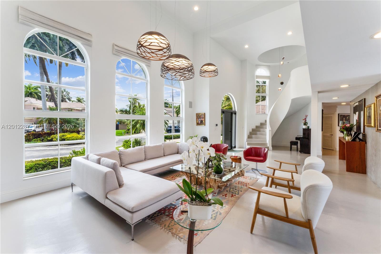 A bright living room features high ceilings, large arched windows, and a curved staircase — 8763 SW 61st Pl, Pinecrest FL 33156, PINECREST, FL