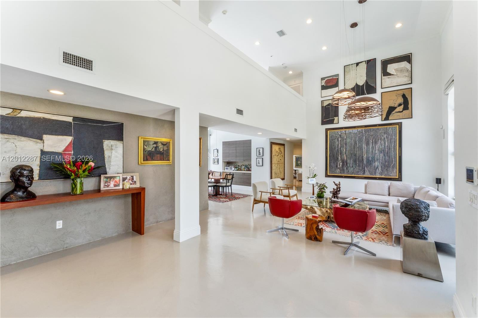 A spacious living room features high ceilings, modern art, red accent chairs, and concrete flooring — 8763 SW 61st Pl, Pinecrest FL 33156, PINECREST, FL