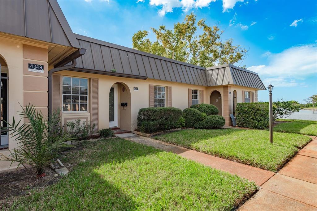 A single-story building with a metal roof, tan stucco walls, and a landscaped front yard — 4347 RUSTIC DRIVE UNIT 4347, NEW PORT RICHEY, FL