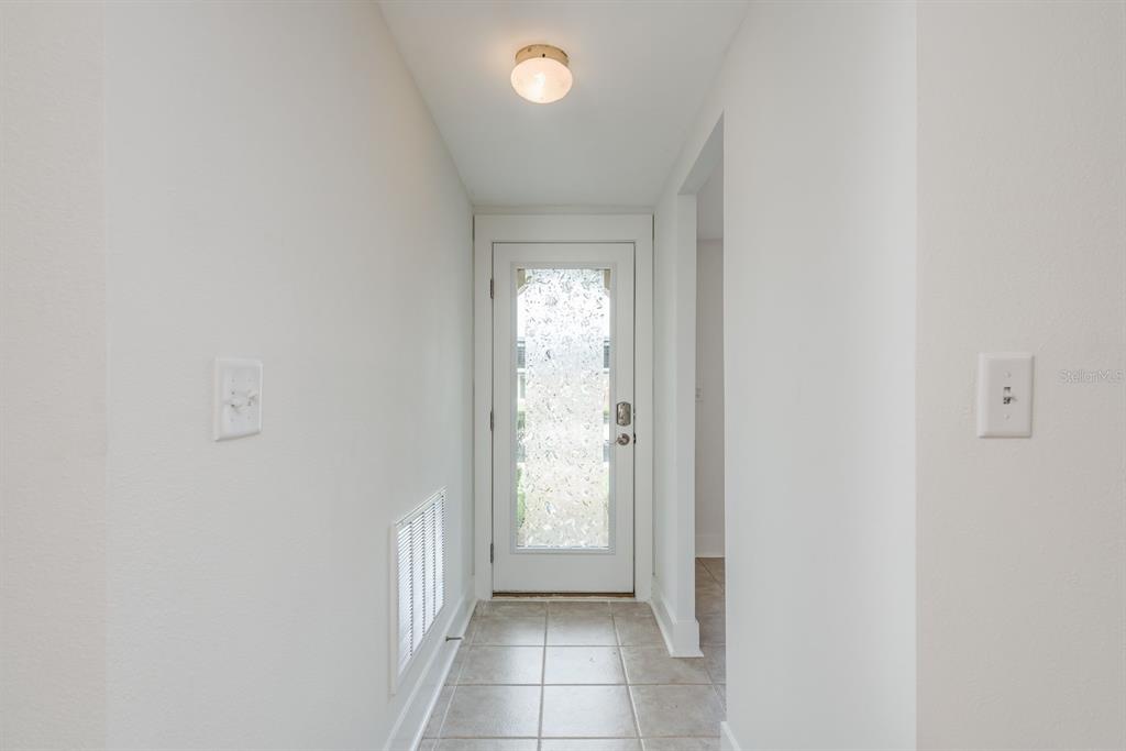 A narrow hallway features tiled flooring, white walls, a ceiling light, and a glass-paneled door — 4347 RUSTIC DRIVE UNIT 4347, NEW PORT RICHEY, FL