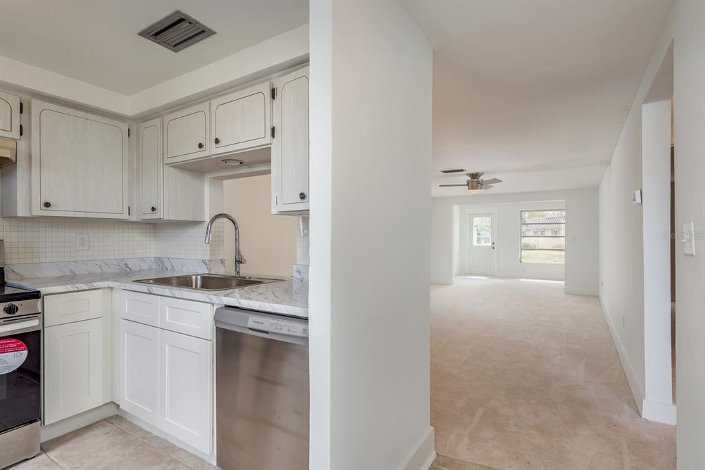 A kitchen with white cabinets and stainless steel appliances opens into a carpeted living area — 4347 RUSTIC DRIVE UNIT 4347, NEW PORT RICHEY, FL