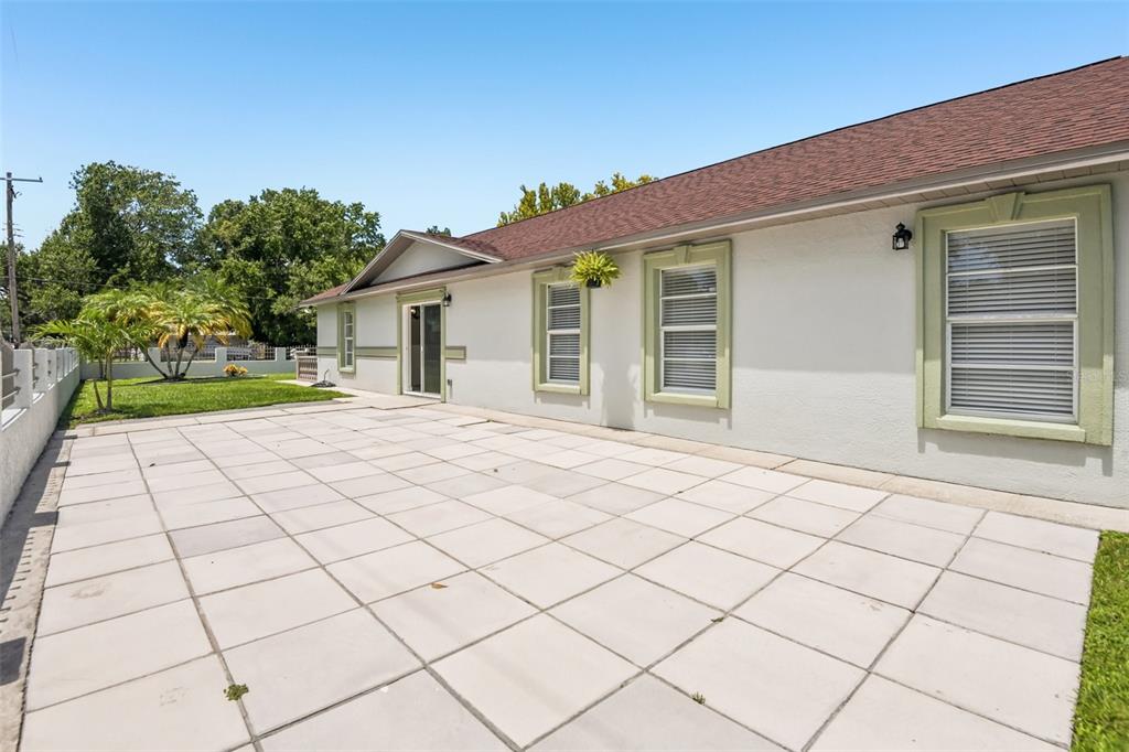 A paved patio sits beside the white exterior wall of a house with green-trimmed windows — 7001 N CLARK AVENUE, TAMPA, FL