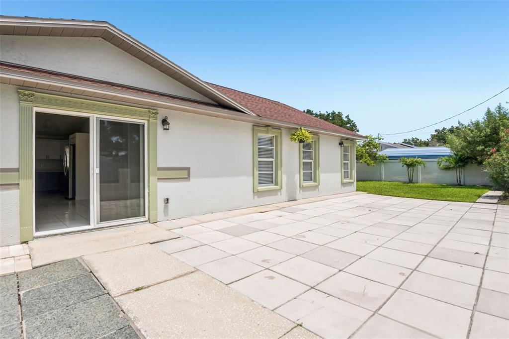 A paved patio extends from the sliding glass doors of a house with light-colored stucco walls — 7001 N CLARK AVENUE, TAMPA, FL