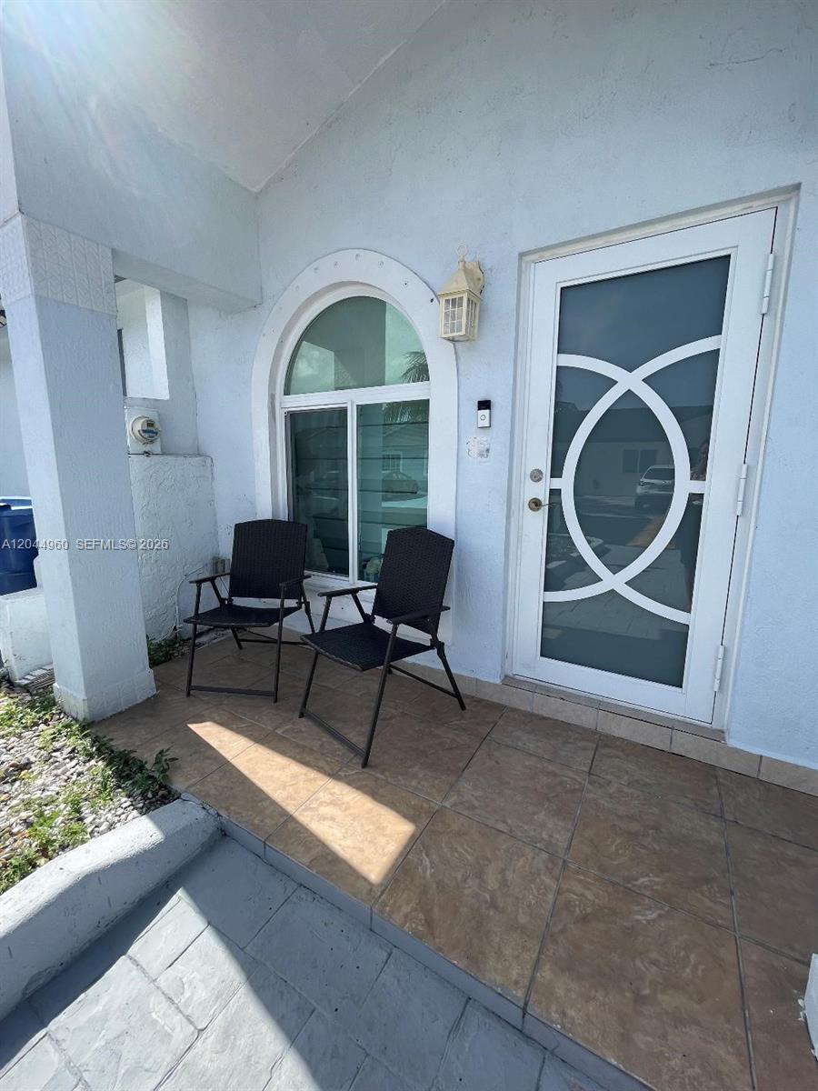 A front porch features two black chairs, a tiled floor, and a decorative arched window — 7681 NW 178th Ter, Hialeah FL 33015, HIALEAH, FL