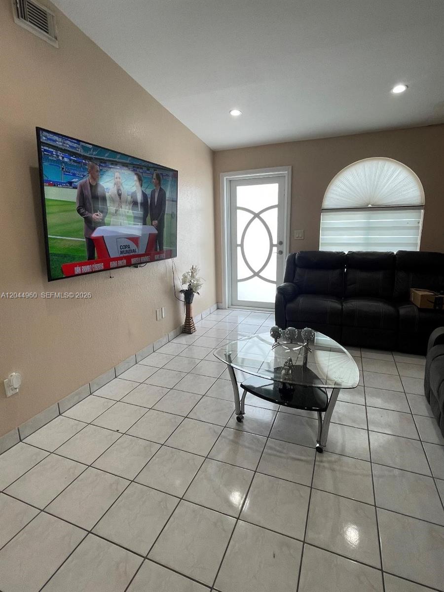A living room features a wall-mounted television, a glass coffee table, and tiled flooring — 7681 NW 178th Ter, Hialeah FL 33015, HIALEAH, FL