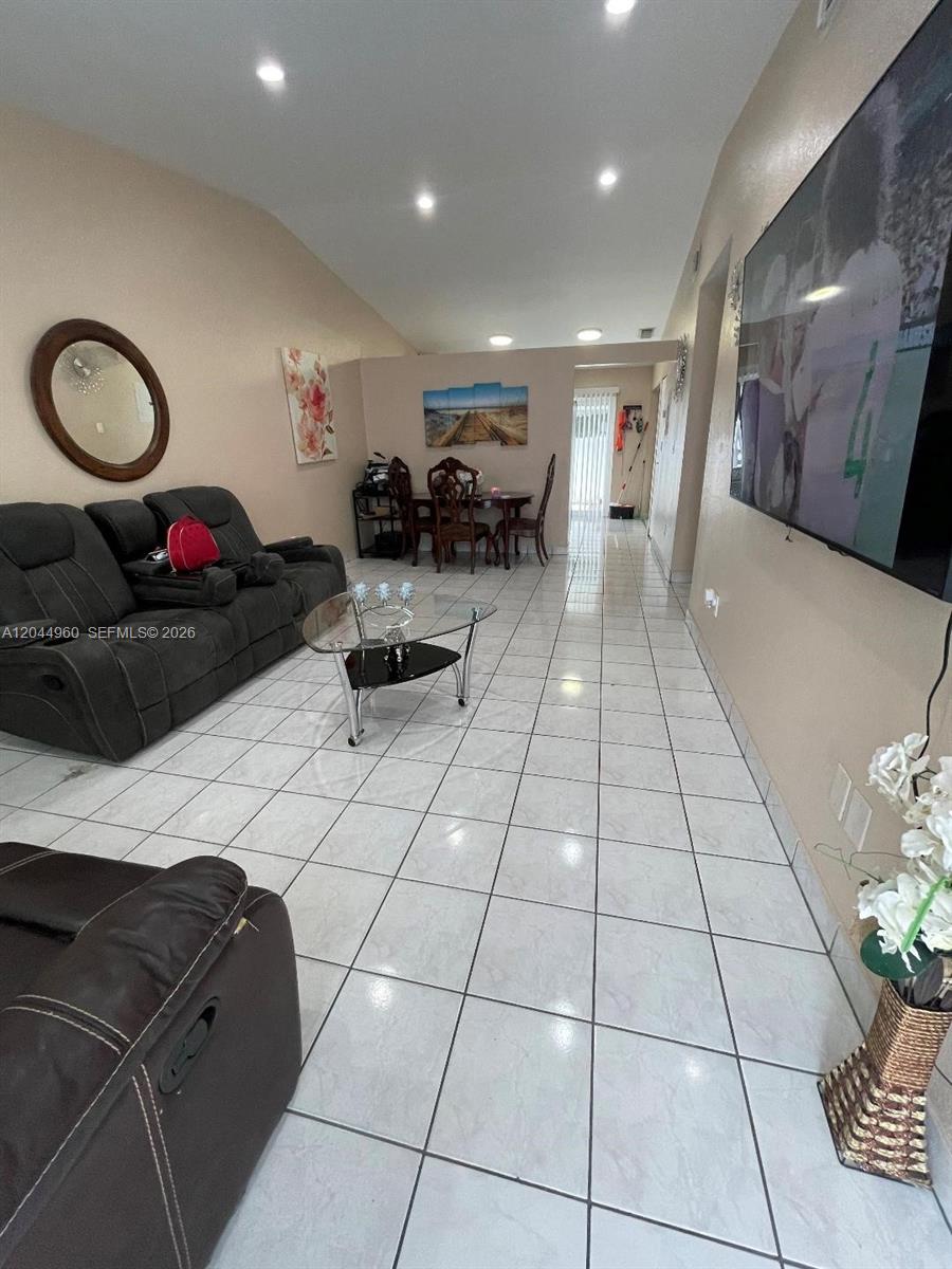 A living room features tile flooring, a dark sofa, a glass coffee table, and dining area — 7681 NW 178th Ter, Hialeah FL 33015, HIALEAH, FL