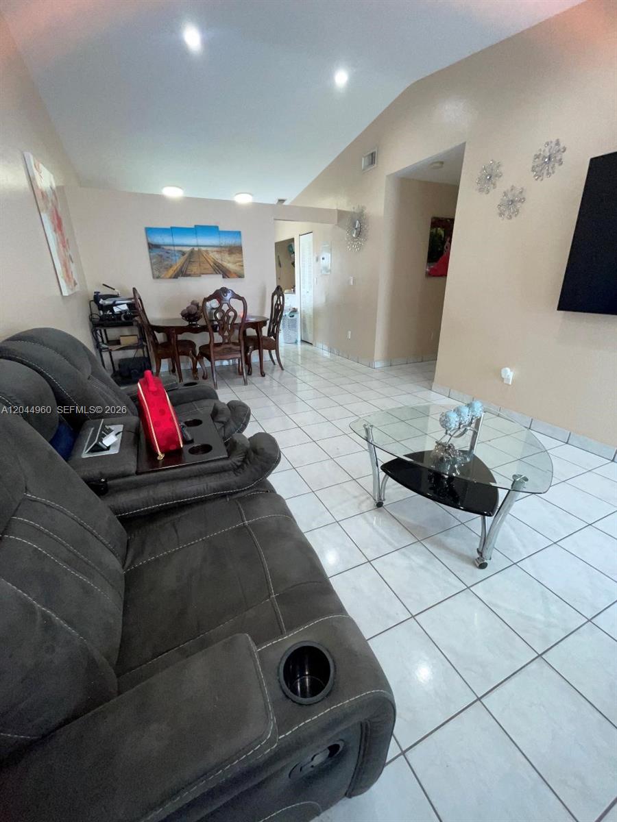 A living room with gray reclining furniture, a glass coffee table, and a dining area — 7681 NW 178th Ter, Hialeah FL 33015, HIALEAH, FL