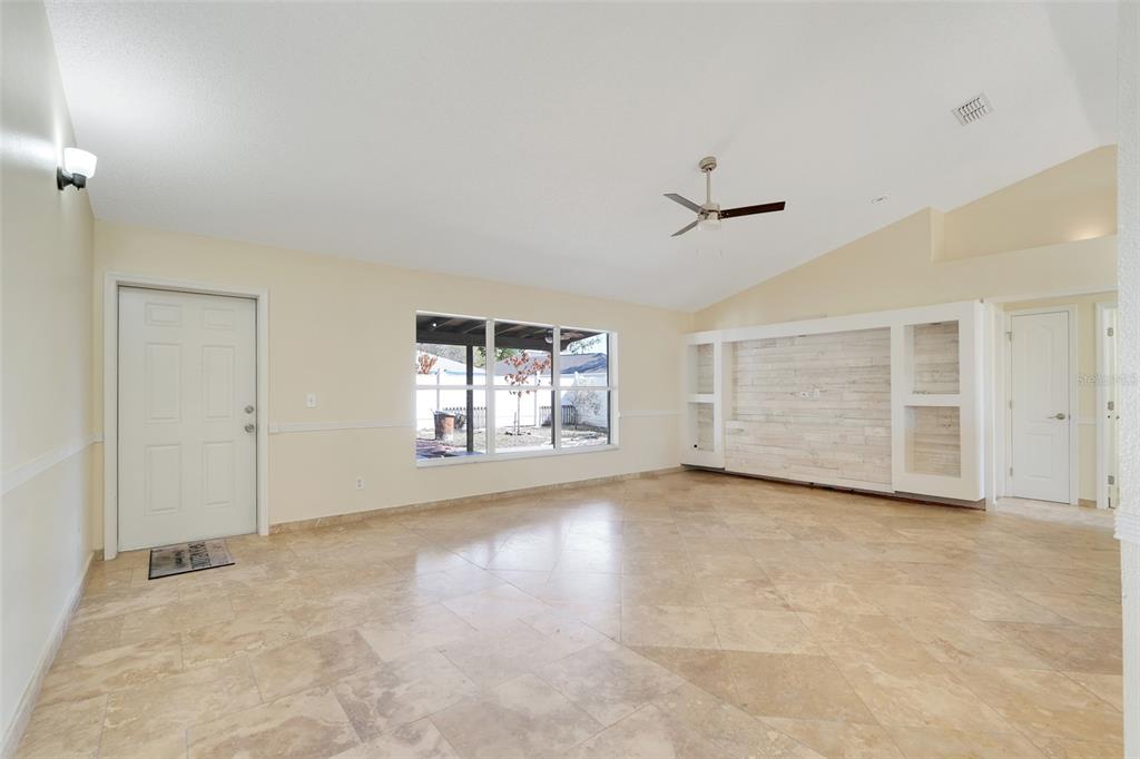 A spacious living room features light-colored tile flooring, a vaulted ceiling, and a built-in wall unit — 617 PARAKEET COURT, KISSIMMEE, FL