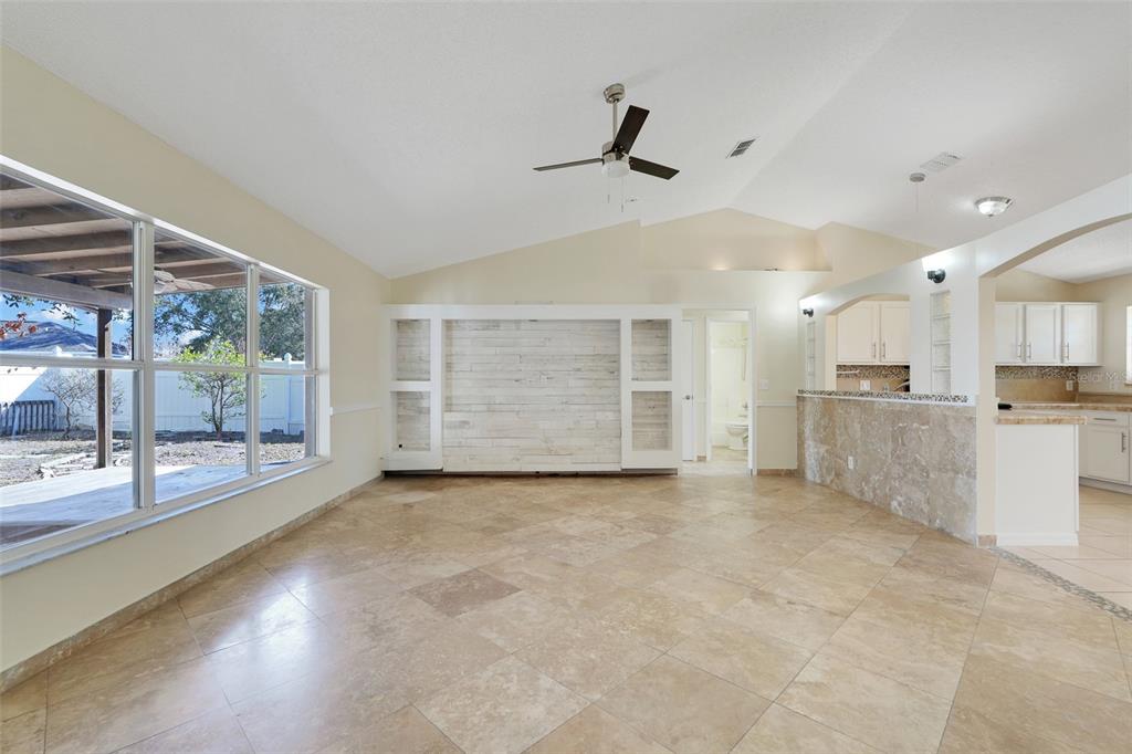 A spacious living room features tile flooring, a vaulted ceiling, and a white accent wall — 617 PARAKEET COURT, KISSIMMEE, FL