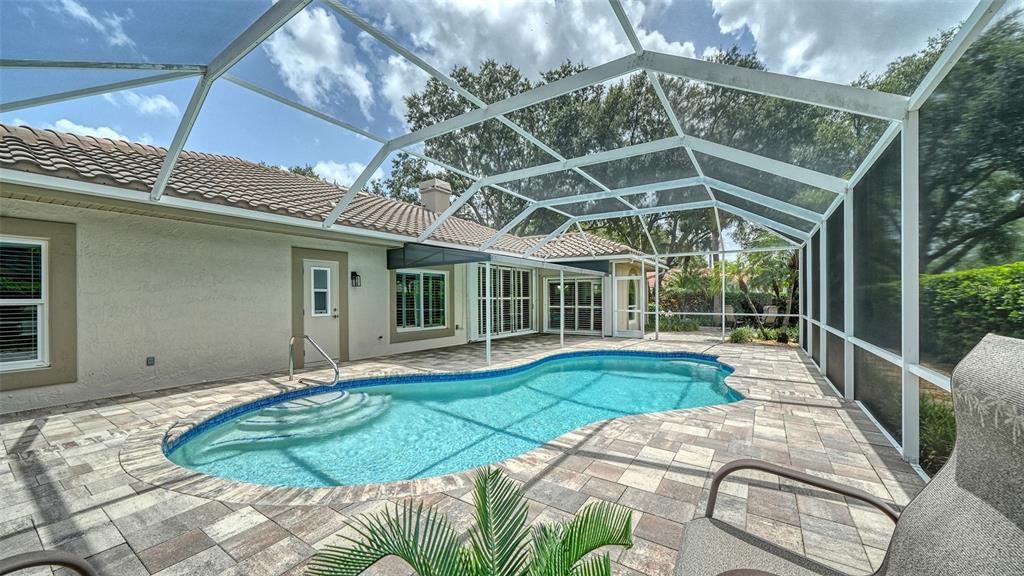 A swimming pool with a paved deck is enclosed by a screened lanai behind a house — 4322 HIGHLAND OAKS CIRCLE, SARASOTA, FL