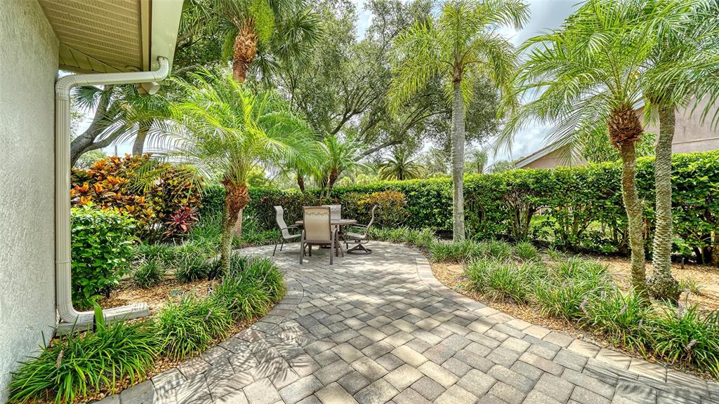 A paved patio with a dining set is surrounded by palm trees and a hedge — 4322 HIGHLAND OAKS CIRCLE, SARASOTA, FL