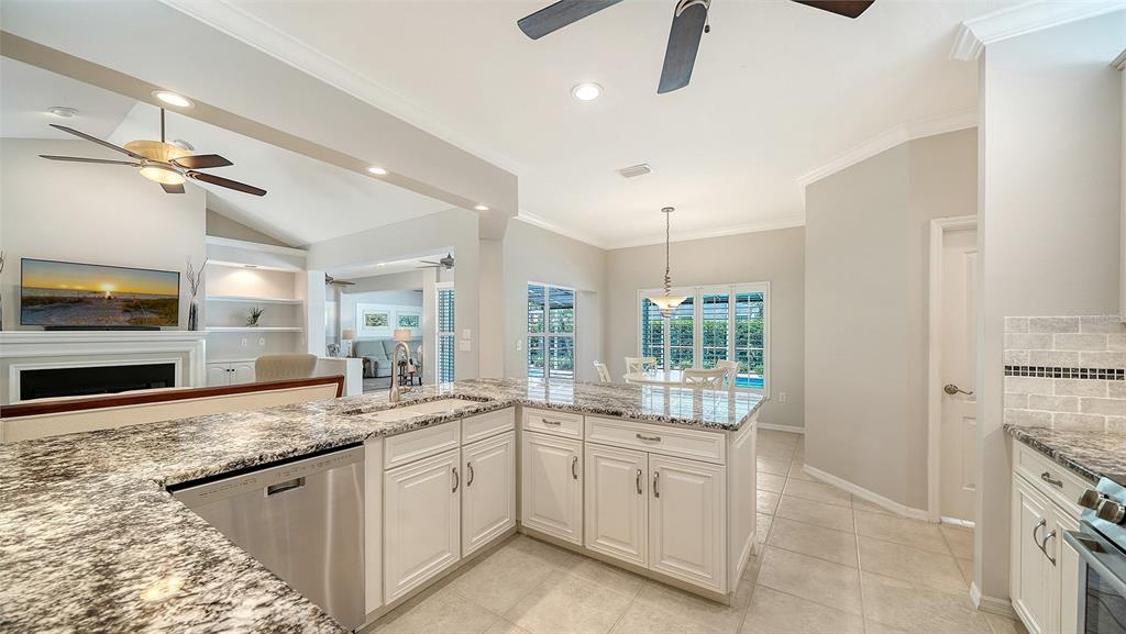 A kitchen with granite countertops and white cabinets overlooks a living area and dining space — 4322 HIGHLAND OAKS CIRCLE, SARASOTA, FL