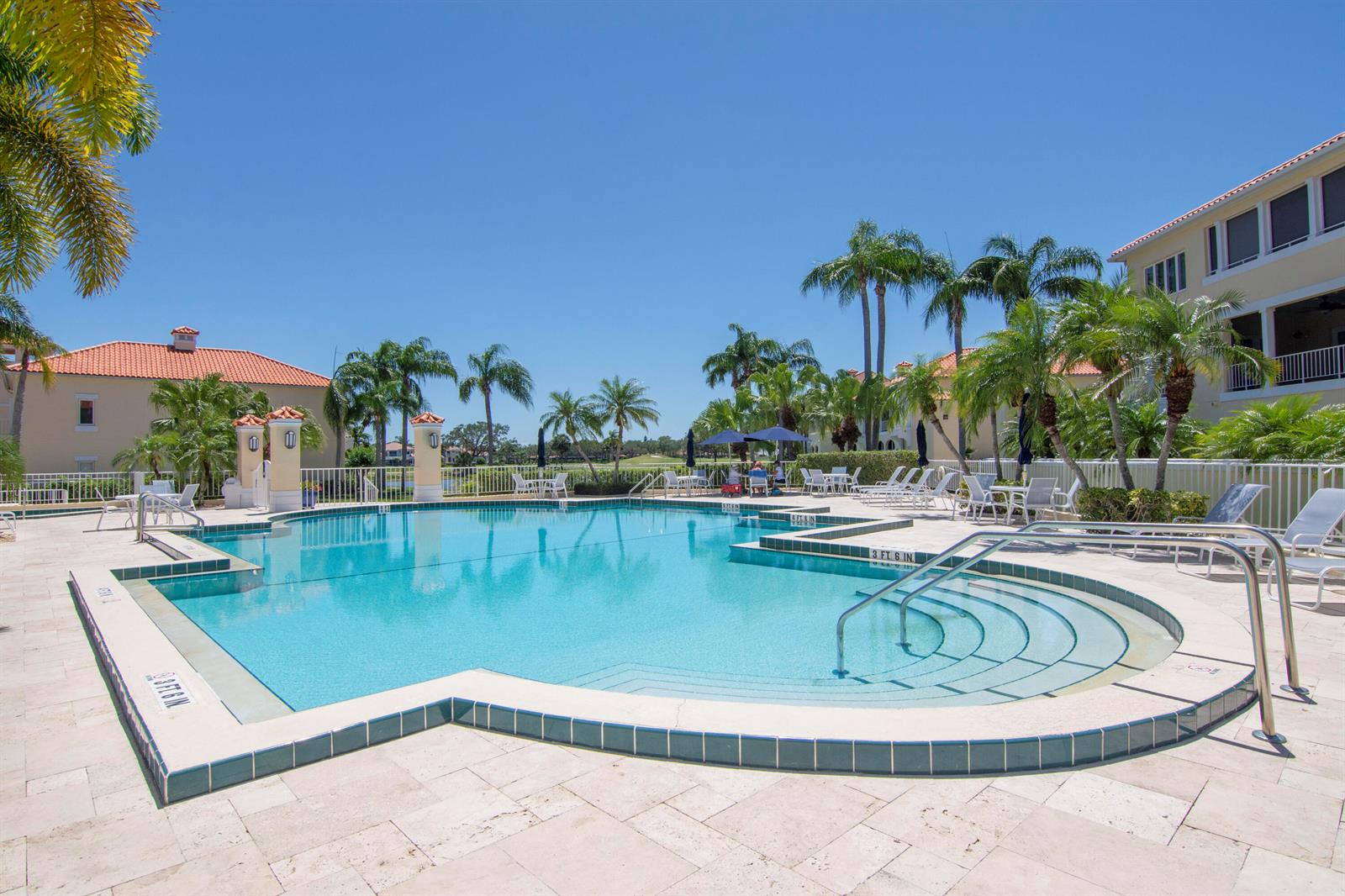 A swimming pool with steps and lounge chairs is surrounded by palm trees and buildings — 5045 Harmony Circle # 209, Vero Beach FL 32967, VERO BEACH, FL