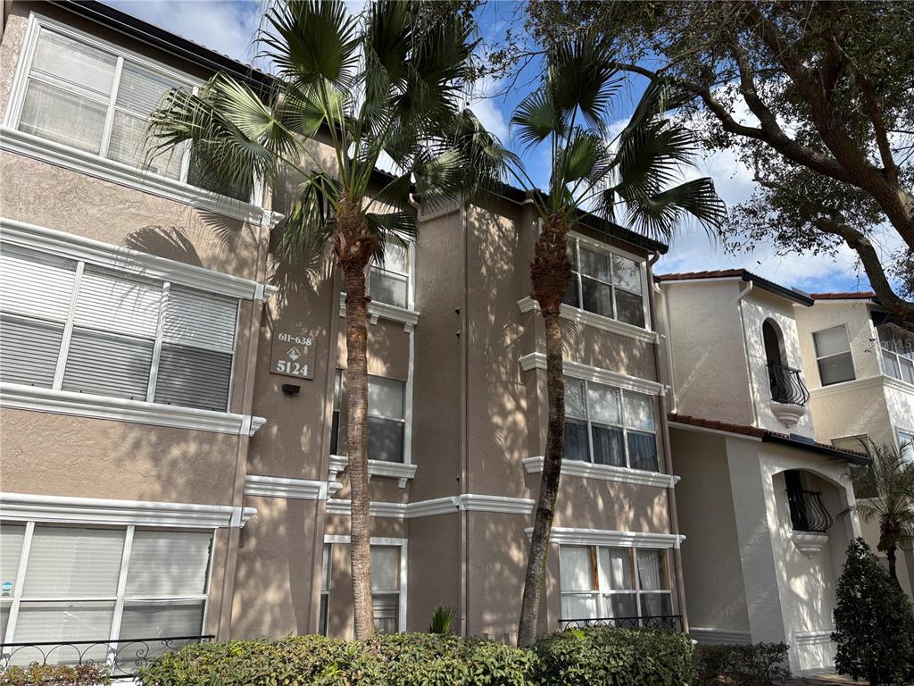 A three-story tan apartment building features two palm trees in front of the entrance — 5124 CONROY ROAD UNIT 623, ORLANDO, FL
