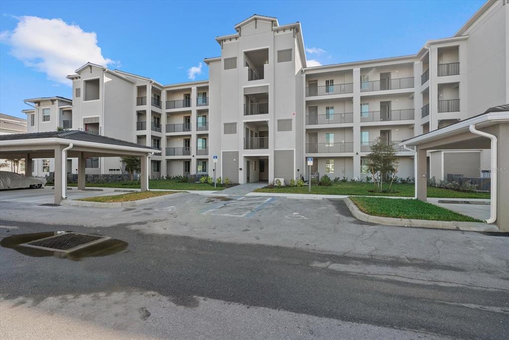 A multi-story apartment building with covered parking spaces and a paved parking lot in front — 17570 OPAL SAND DRIVE UNIT 302, VENICE, FL