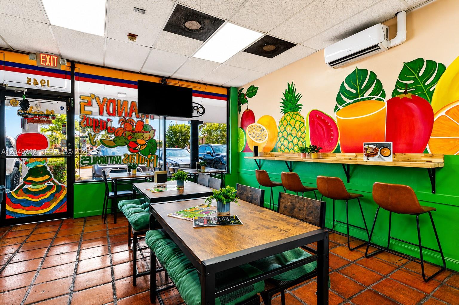 A restaurant interior features wooden tables, bar seating, and a colorful fruit mural on the wall — HIALEAH, FL