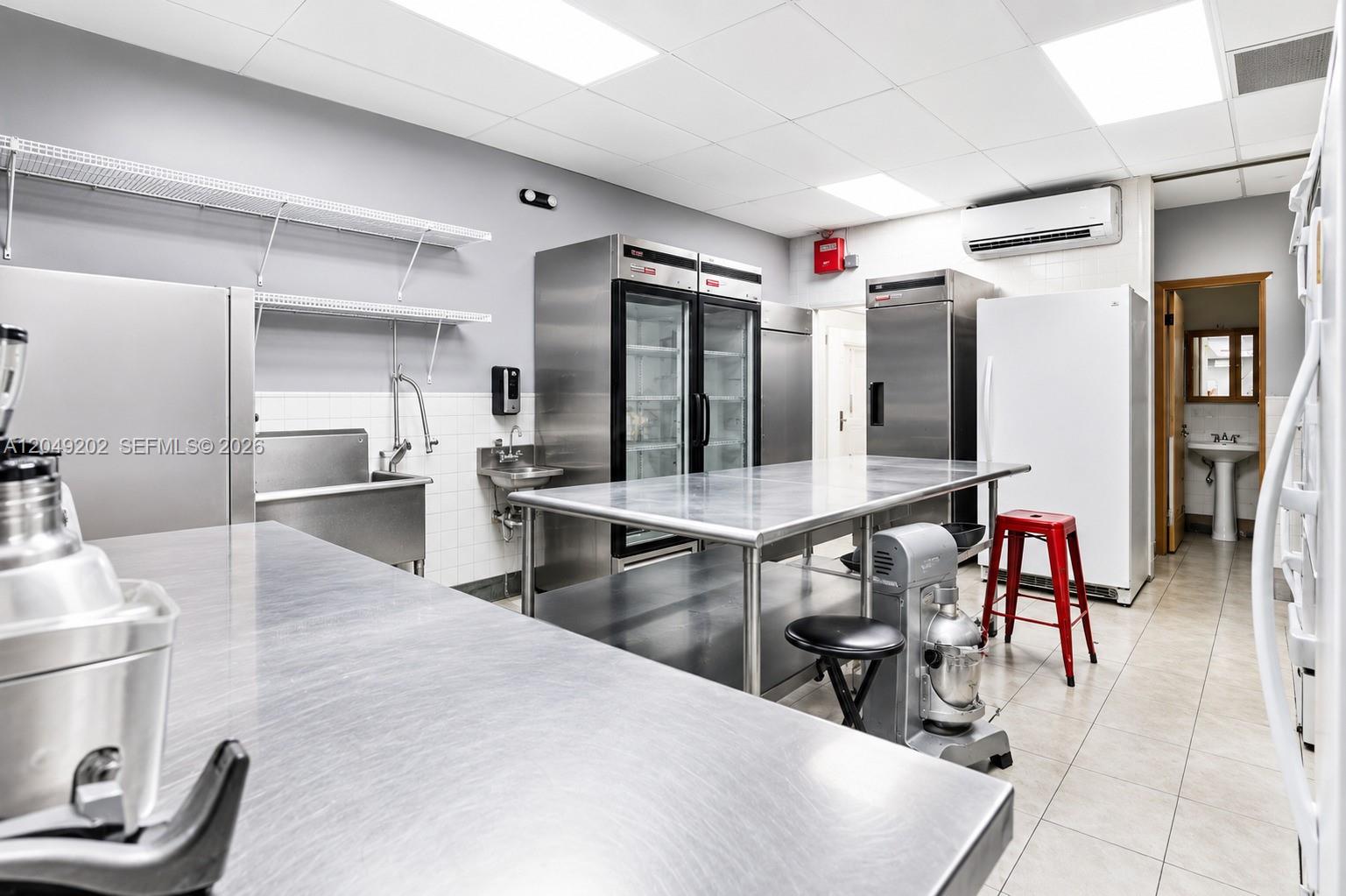 A commercial kitchen features stainless steel prep tables, industrial refrigerators, and a tiled floor — HIALEAH, FL