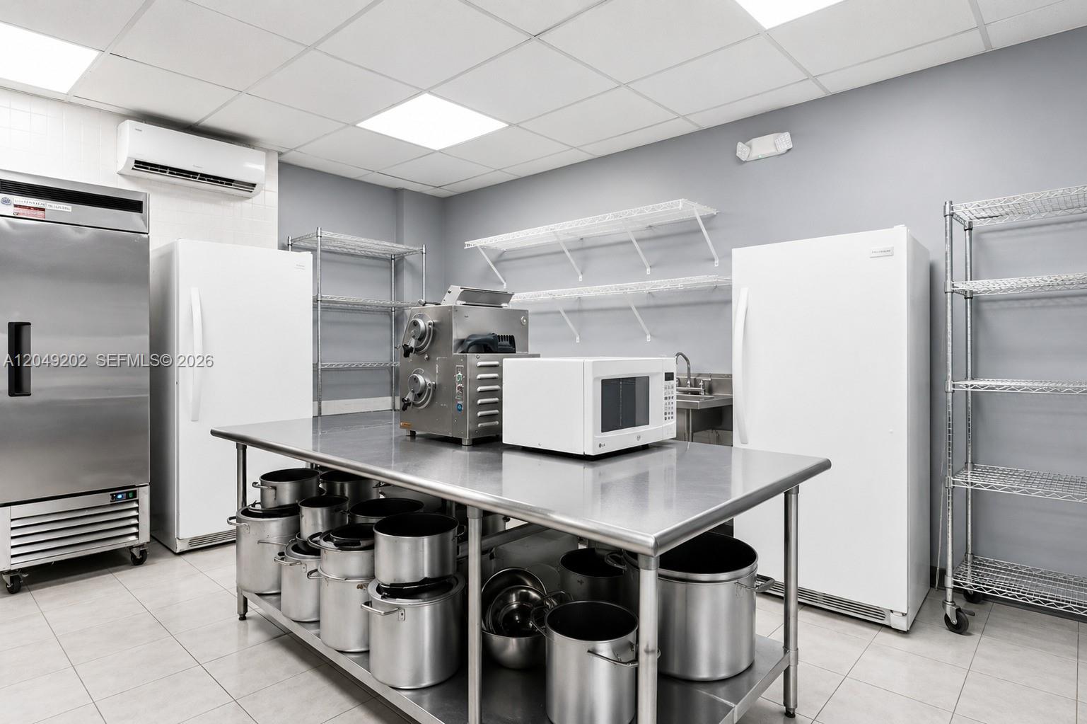 A commercial kitchen features stainless steel appliances, metal shelving, and a central prep table — HIALEAH, FL